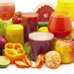 alt="Conjunto de jugos naturales en copas finas, rodeado de frutas y verduras de variuos colores, y algunas casacaras de frutas, todo en tono rojo, amarillo y verdes"