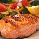 alt="Plato de comida con un buen fillete de salmon a la parrilla en la parte frontal, detras verduras y especias de varios colores"