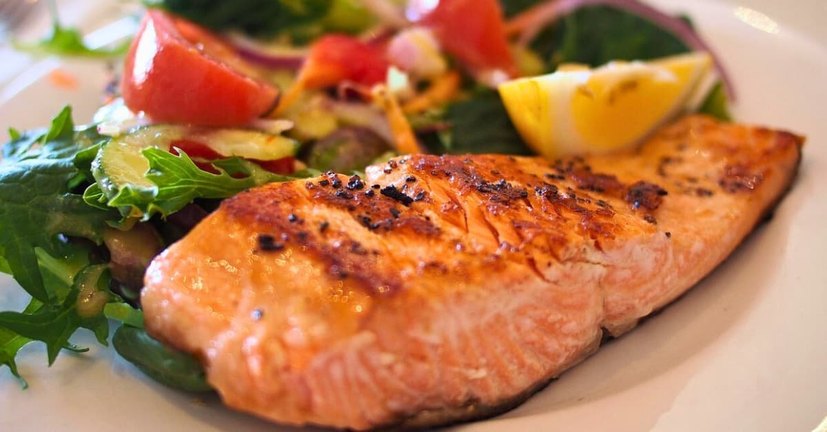 alt="Plato de comida con un buen fillete de salmon a la parrilla en la parte frontal, detras verduras y especias de varios colores"