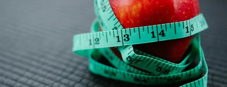 alt="sobre una suerfiecie corrugada, se ve una manzana super roja, que esta siendo cubierta por una cienta metrica de color verde turqueza,dandole vueltas de abajo a arriba"