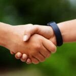 alt="Con fondo de naturaleza borrosa se ven dos manos amigas estrechandose como saludo"