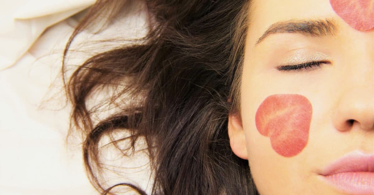 alt="Rostro de mujer con pelo suelto y corazones pintados en su cara"