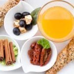 alt="Desayuno saludable en plato cuadrado blanco, frutas, yogures, jugos naturales y tostadas de pan"