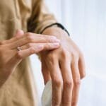 alt="Hombre delgado tocandose la parte superior de una mano como si le doliera algo"