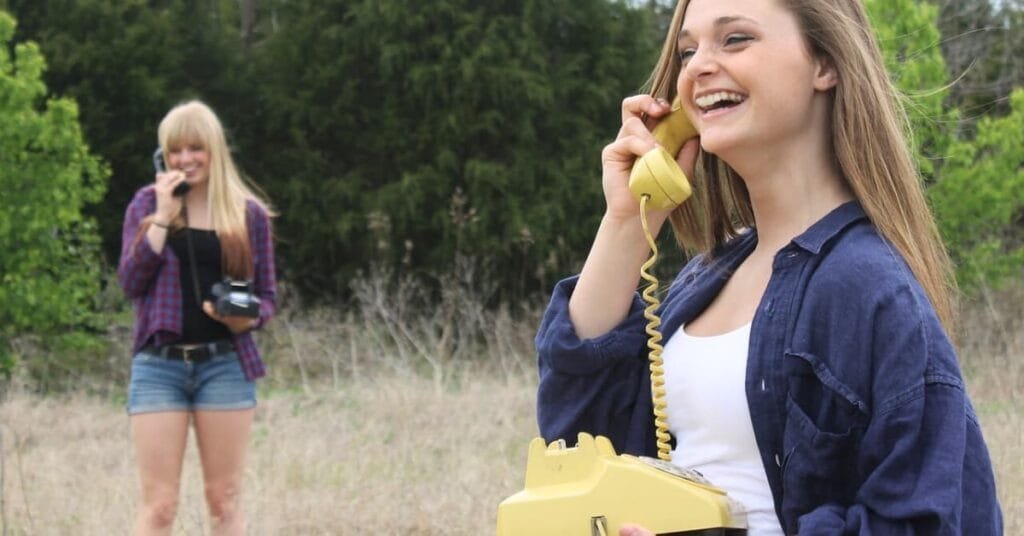 alt="Dos amigas conversando por telefonos antiguos en medio del campo"