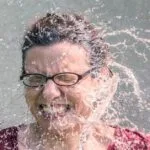 alt="Mujer Con gafas de ver siendo mojada por valde de agua fria"