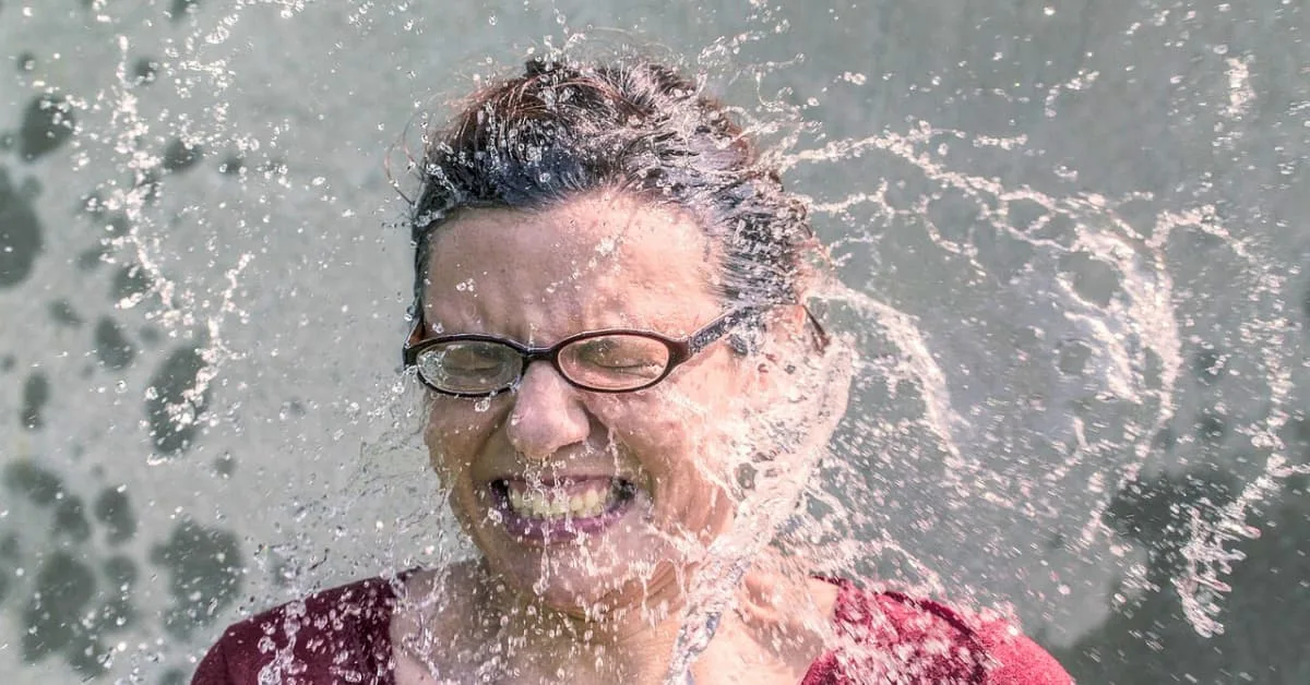 alt="Mujer Con gafas de ver siendo mojada por valde de agua fria"
