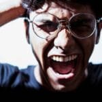 alt="Con las manos en la detras de la cabeza y griitando desesperado aprece en una habitacion vacia un hombre joven con una camiza verde,,lleva puesto unos Espejuelos de leer y un reloj"