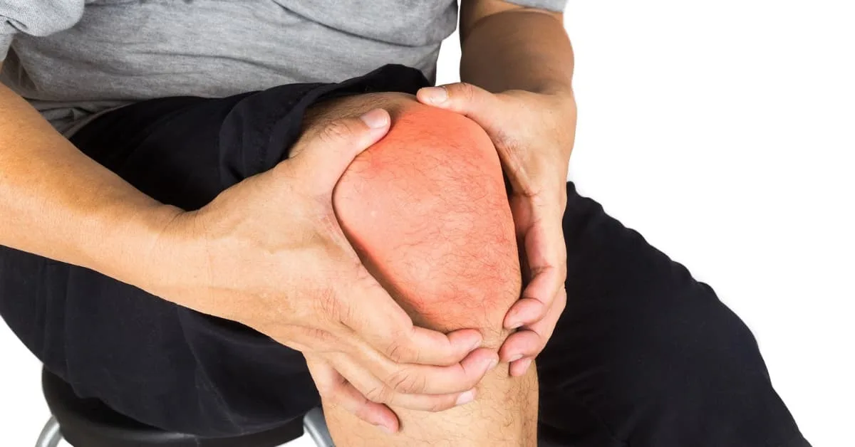 alt="Hombre con ropa deportiva, sentado abrazando la rodilla con las dos manos mientras se lamenta por el dolor"